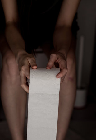 Woman sitting on the toilet and holding toilet paper in her hands. constipation and stomach problemsの写真素材