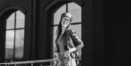 Portrait of young beautiful trendy girl in stylish sunglasses and leather jacket posing on the streetの写真素材