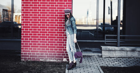 Full length portrait of trendy woman standing at the brick wall. Urban Fashion Concept. copyspace.の写真素材