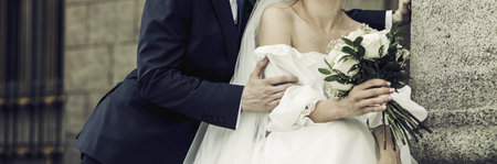 wedding couple embracing after wedding ceremony in city. Elegant bride and groom with wedding bouquetの写真素材