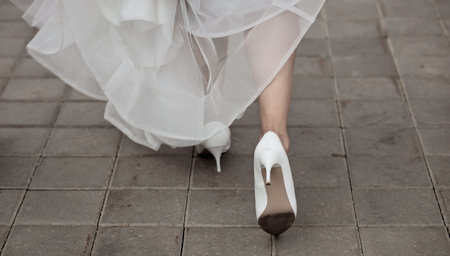 Bride's legs in stylish high heels peek out from under the wedding dress, close-upの写真素材