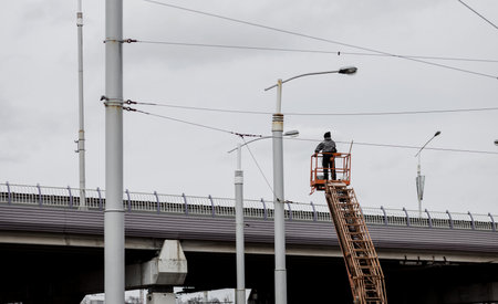 Worker in at height wearing and safety harness. Height construction worker against sky. Electrician standing in mobile crane bucket and rising to repair street wiringの写真素材