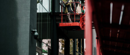 Female window cleaner cleaning glass windows on modern building high in the air on a lift platform.の写真素材