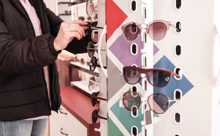 woman chooses sunglasses on a shelf in a store. A stand with glasses in an optics storeの写真素材