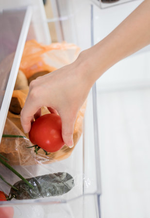 a woman's hand takes a red tomato from the refrigerator. the concept of healthy nutritionの写真素材
