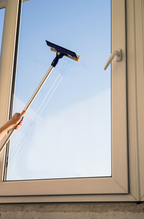 Hand with mop washes the glass of the windows. Concept for home cleaning servicesの写真素材