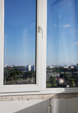 new modern white plastic pvc window with frame and handle and view on blue sky with clouds.