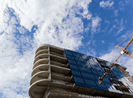 Tower crane near contemporary skyscraper with shiny glass facade at construction site against clear blue sky on sunny dayの写真素材