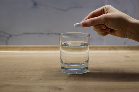 Woman hand putting tablet to the glass of water on wooden table.の写真素材