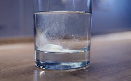 Fizzy tablet in glass of water on wooden tableの写真素材