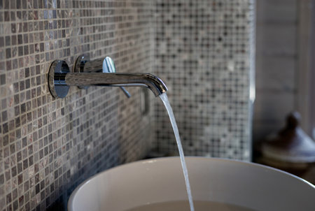 Minimalist Chrome Faucet in Gray and Beige Against Mosaic Tile. Luxury Decor in Bathroomの写真素材