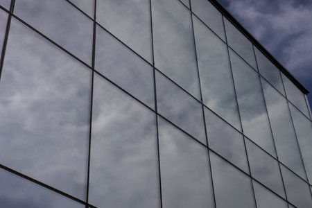 Modern glass building facade with cloudy sky reflectionsの写真素材