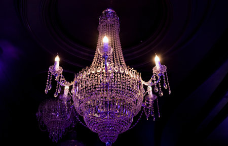 Elegant Crystal Chandelier Hanging from Ceiling Against Dark Backgroundの写真素材
