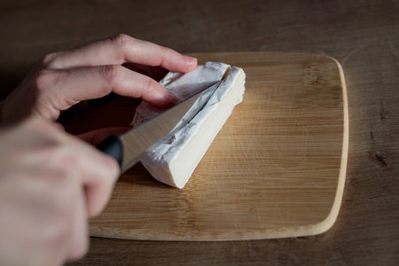 Female hand cutting camembert on wooden board. food preparation