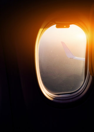 Majestic view through window of wing of plane while jet flying high against sky in sunsetの写真素材