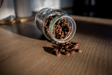 Coffee beans, poured from a glass transparent jar on wooden table. selective focusの写真素材