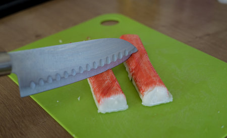 Close-up of hand cutting crab sticks on plastic boardの写真素材