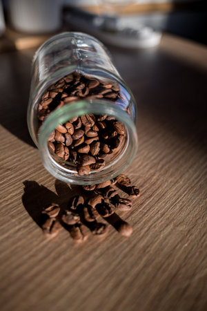 Black coffee beans poured from glass jar on a wooden table. selective focusの写真素材
