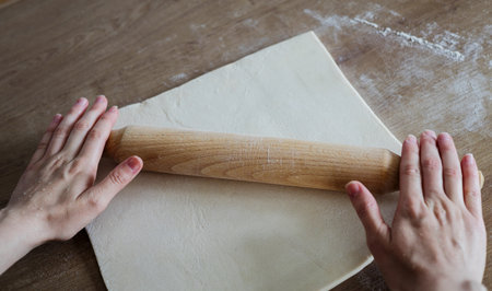 Person handling a dough with a rolling pin floured wooden tableの写真素材