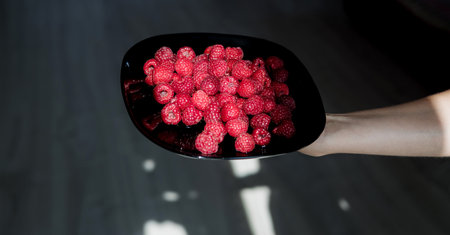 hand holds a black plate with raspberries. Delicious and Healthy Foodの写真素材