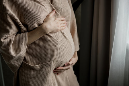 Young beautiful woman in second trimester of pregnancy. Close up of pregnant female with arms on her round belly. Expecting a child conceptの写真素材
