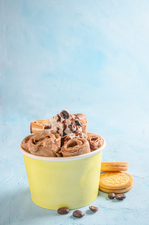 Ice cream roll of chocolate and coffee, with pieces of chocolate and cookies on blue background