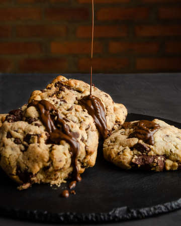 Chocolate chip cookies with chocolate syrup, on black background and brick wallの写真素材