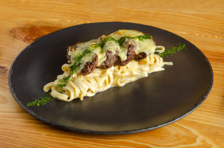 Linguini a la Routa with extra tenderloin, sprinkled with parsley and served on a black plate on a wooden table.の写真素材