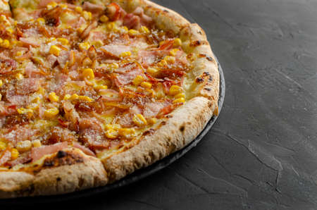 Ham and corn pizza prepared in a wood-fired oven. Black background. Parmesan cheese.の写真素材