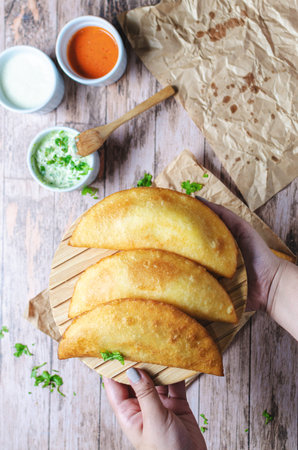 Girl's hands with empanada typical food from Venezuela adding gasacaca sauce, trio sauce, woodwn tableの写真素材