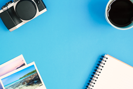 Desk above, top view of   vintage camera, a glass of coffee, notepad, and instant photo frames on blue backgroundの写真素材