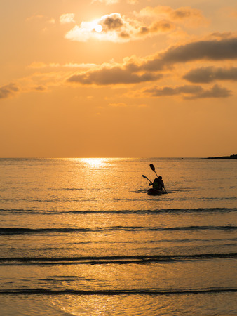 Silhouette of a lovely couple on a canoe boat during sunset.   Silhouette of two people on a kayak at sea beach at twilight timeの写真素材