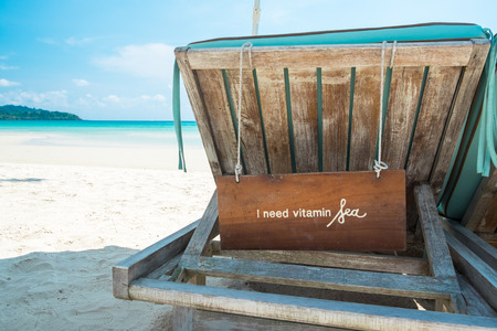A wooden label with text " I need vitamin Sea " hanging behind the beach bed on a sunny day at the sea beachの写真素材