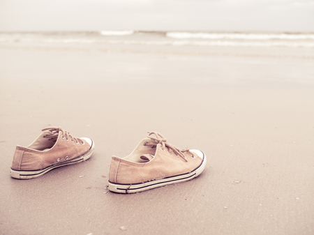 Yellow vintage canvas shoes on the sand beach in vintage filter tone - canvas shoes at the sea beachの写真素材