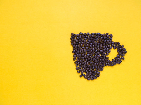 Coffee beans arrange in a coffee cup on yellow background with copy space
