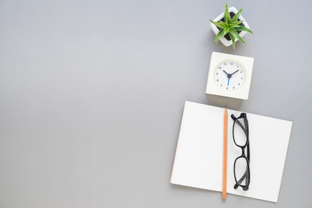 Top view of open empty notebook with pencil, eyeglasses, clock, and plant on grey  office desk backgroundの写真素材
