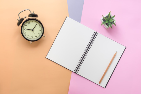 Top view of open empty spiral notebook with pencil, vintage clock, and plant on pastel colorful backgroundの写真素材