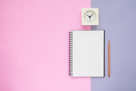 Top view desk above of open empty spiral notebook with pencil and white alarm clock on pastel colorful backgroundの写真素材