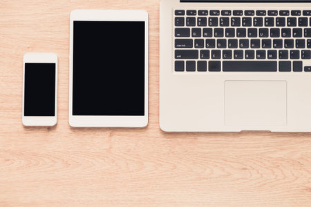 Top view of office desk - laptop, mobile phone, and tablet on wooden table
