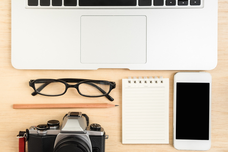 Table top view of laptop, vintage camera, mobile phone and stationery items on wooden backgroundの写真素材