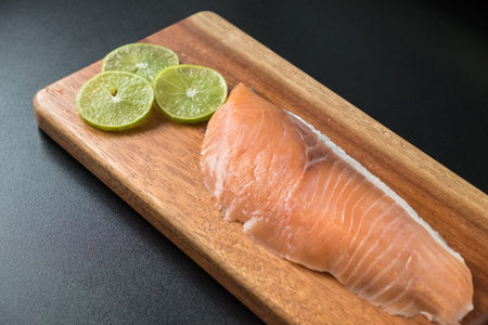 Selective focus on fresh salmon on wooden tray with sliced green lemonの写真素材