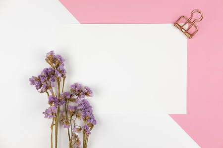 Top view of white empty paper with paper clip and violet statice flower bouquet on pastel white and pink backgroundの写真素材