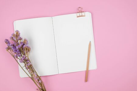 Top view of dot grid notebook with pencil, paper clip and violet statice flower bouquet on pastel pink backgroundの写真素材