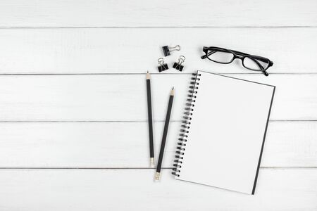 Top view of minimal office desk with an open blank notebook, pencils, paper clips and eyeglasses on white wooden backgroundの写真素材