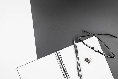 Top view of an empty open notebook with black pencil and eyeglasses on black and white backgroundの写真素材