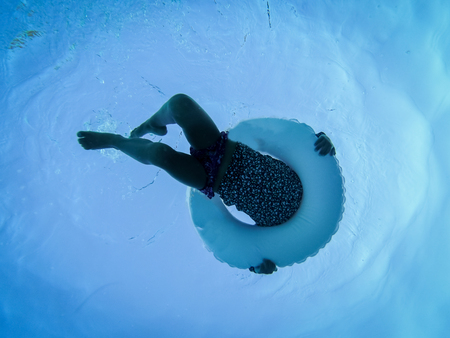 underwater photo of girl swimming in pool with circular floating buoy, unrecognizable