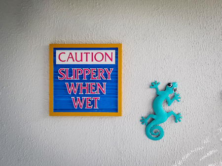 sign saying slippery when wet, caution. typical craft artwork depicting 
 blue green chameleon nexto to singの写真素材