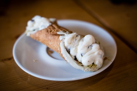 Cannoli with vanilla cream on small whitedish, wooden table. Closeup, blurredの写真素材