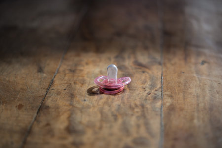 pink pacifier on wooden table, side artificial lighting