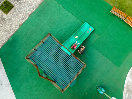 Drone top view of playground in park. We can see a slide and other childrens toys, surrounded by...